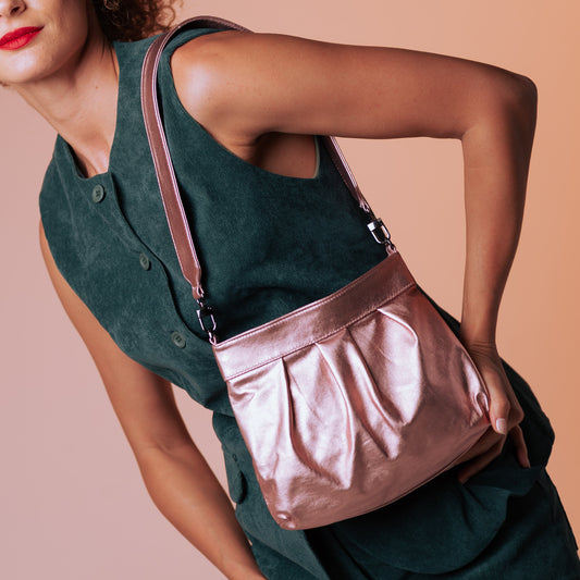 Woman wearing a green outfit with a rose gold handbag against a beige background