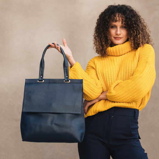 Woman holding a blue handbag against a beige background navy blue leather bag