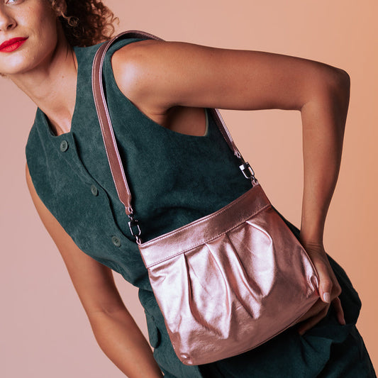 Woman wearing a green outfit with a rose gold handbag against a beige background
