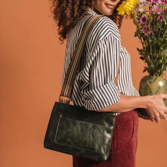 Woman holding a green bag and a vase of flowers against an orange background