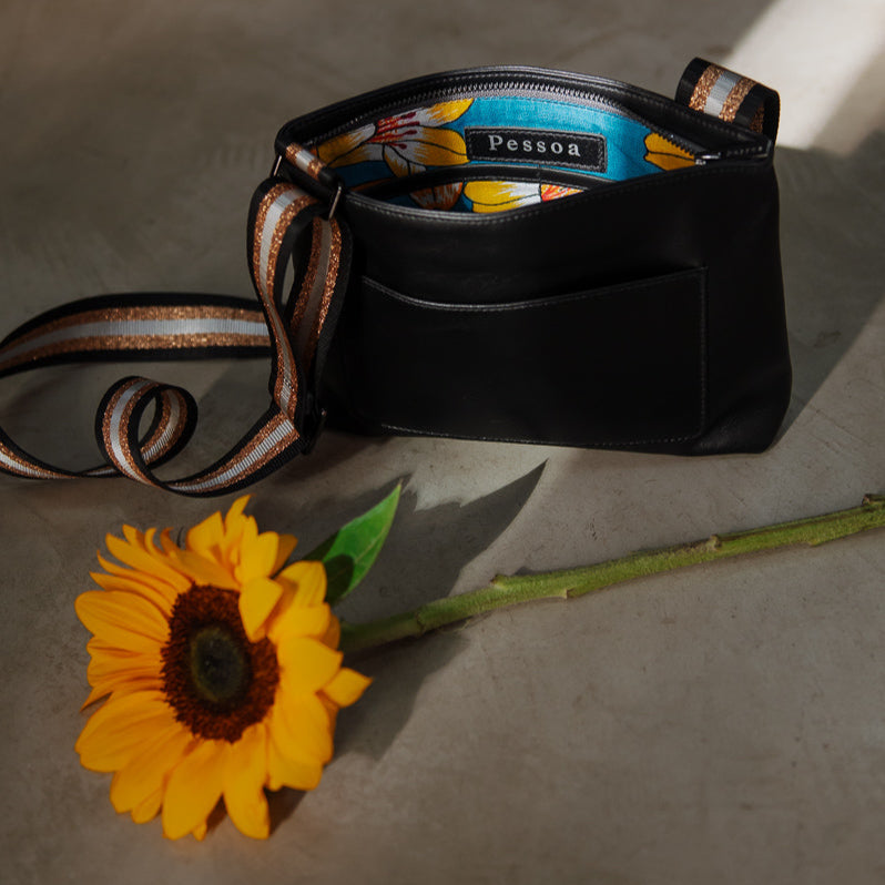 Black handbag with floral design on a textured surface next to a sunflower