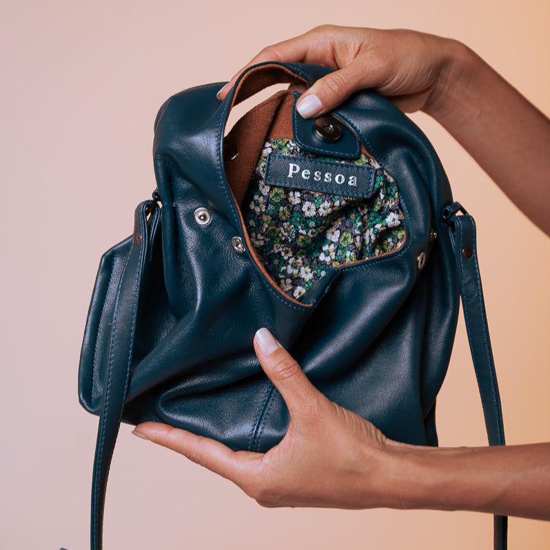 Person holding a blue leather handbag with floral interior lining on a beige background
