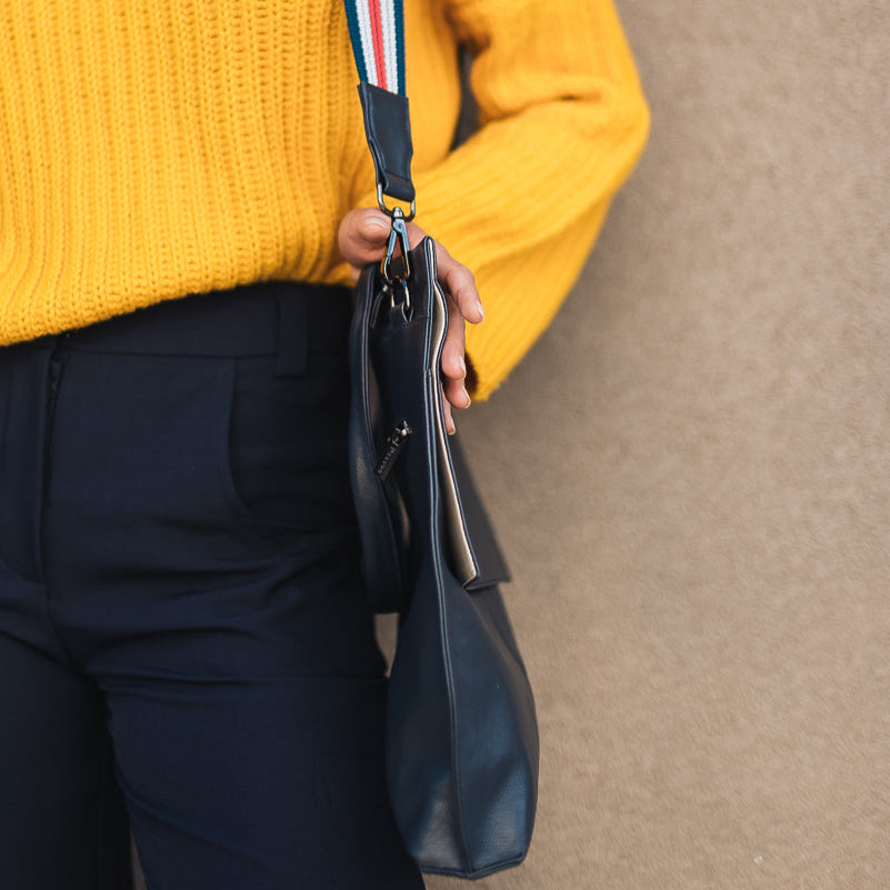 Person wearing a yellow sweater holding a black handbag with a colorful strap against a beige background