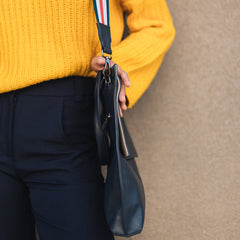 Person wearing a yellow sweater holding a black handbag with a colorful strap against a beige background