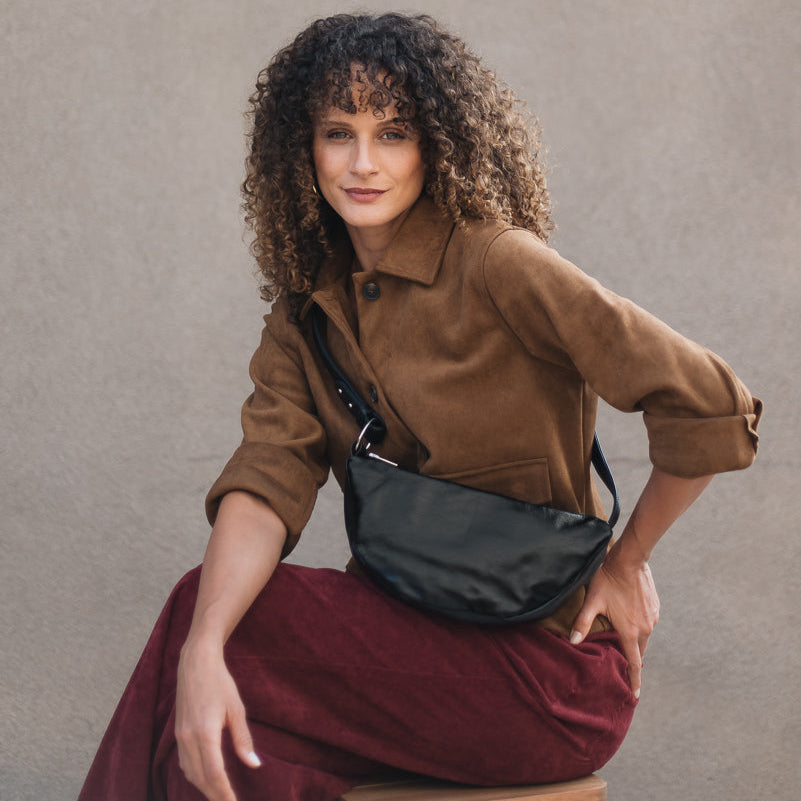Woman sitting on a chair wearing a brown jacket and red skirt with a black bag.