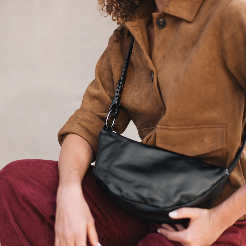 Woman holding a black handbag wearing a brown jacket and red pants against a neutral background