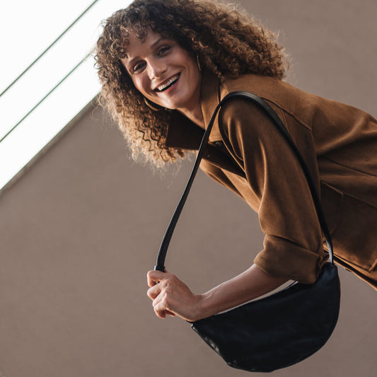 Woman with curly hair holding a black bag against a neutral background