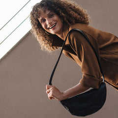 Woman with curly hair holding a black bag against a neutral background