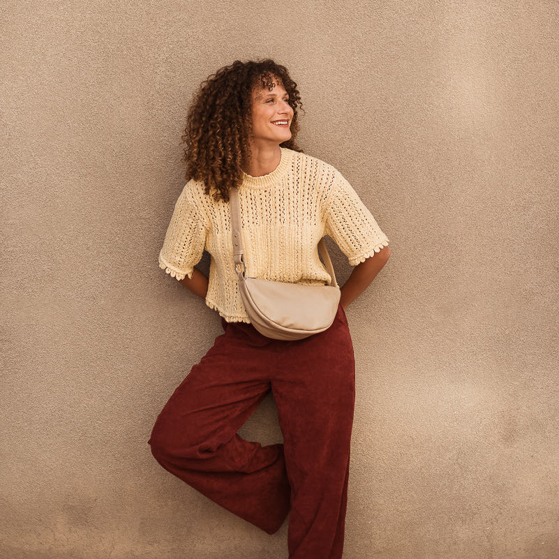 Woman in a beige top and red pants standing against a beige wall