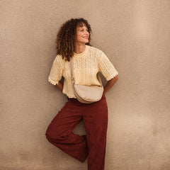 Woman in a beige top and red pants standing against a beige wall