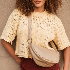 Woman wearing a beige knit top and red pants with a beige fanny pack against a neutral background