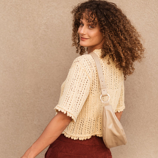 Woman wearing a beige crochet top and maroon pants against a beige background
