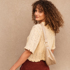Woman wearing a beige crochet top and maroon pants against a beige background