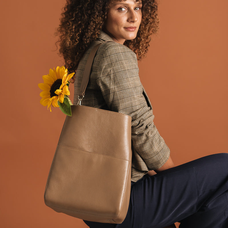 Woman holding a brown leather bag with a sunflower against a brown background