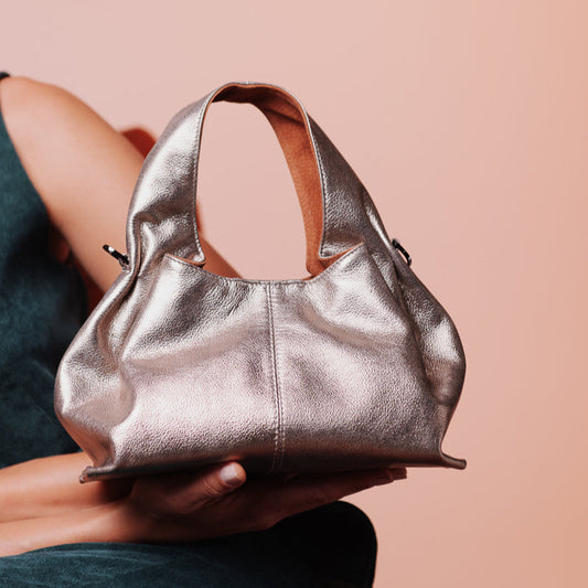 Silver handbag held by a person against a beige background
