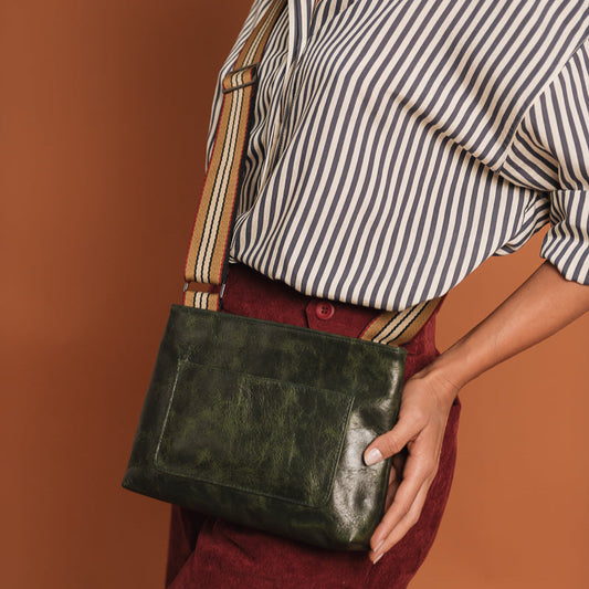 Person holding a green leather bag against a brown background, green leather bag