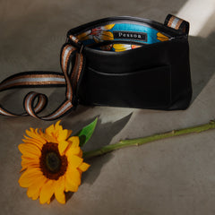 Black handbag with floral design on a textured surface next to a sunflower