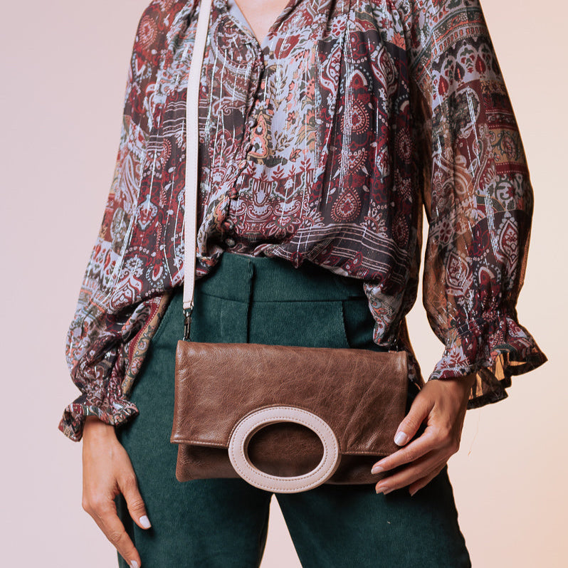 Person wearing a patterned blouse and holding a brown clutch against a plain background