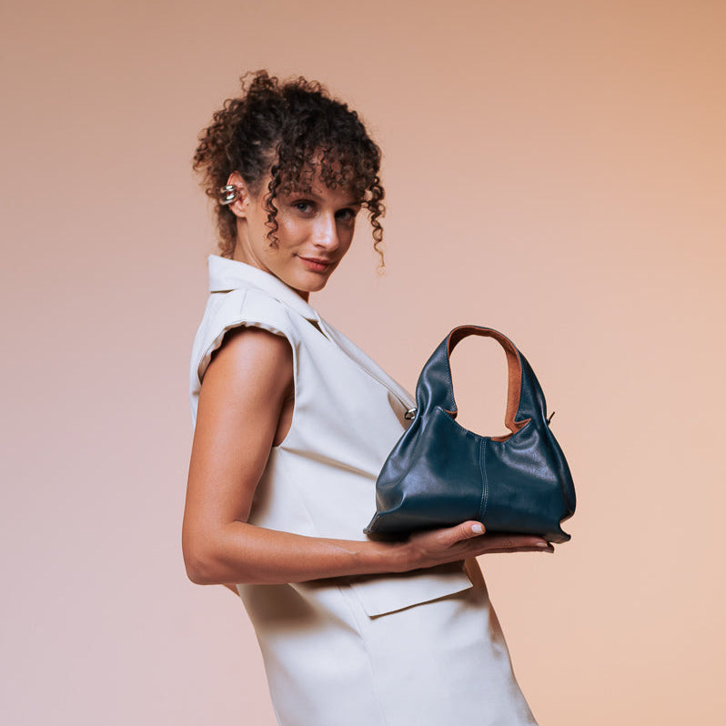 Woman holding a blue handbag against a beige background blue leather