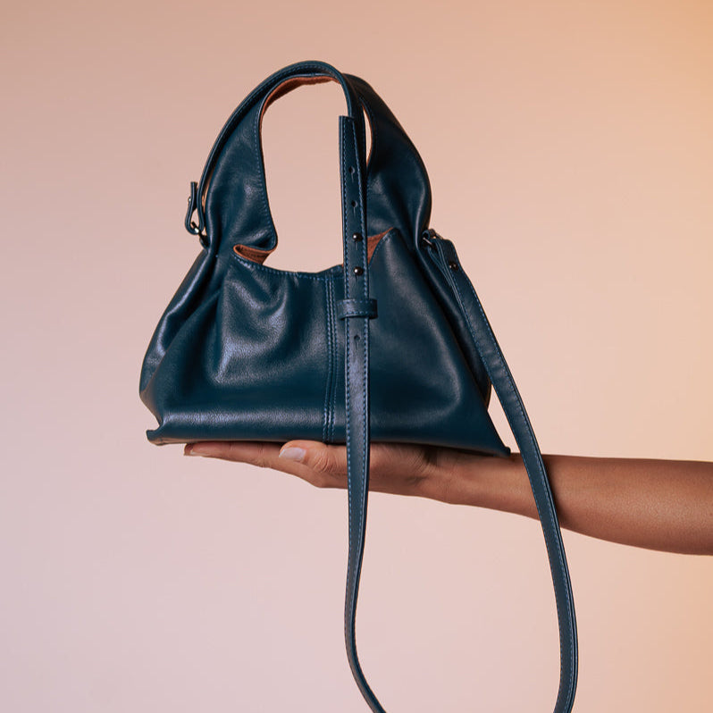 Blue leather handbag held by a person against a beige background