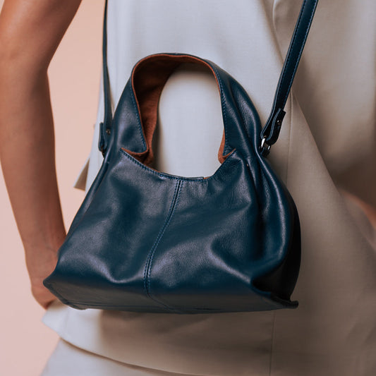 Person wearing a navy blue leather handbag with a brown interior on a beige background
